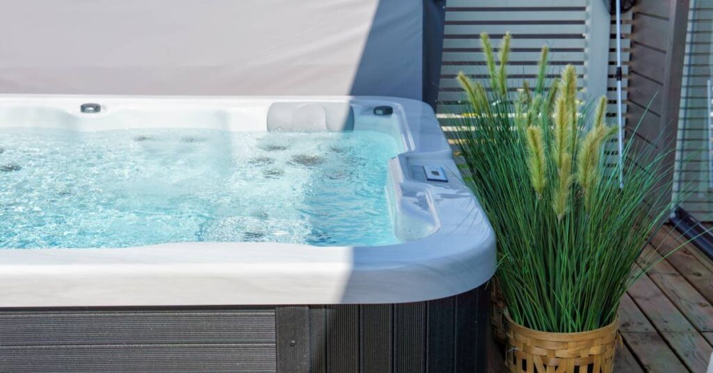 A hot tub with faux wooden siding that is full of bubbles, placed next to a green plant on a home's outdoor deck.