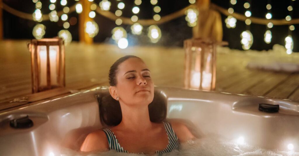 A woman wearing a striped bathing suit in an outdoor spa at night. Warm string lights and lanterns surround the space.