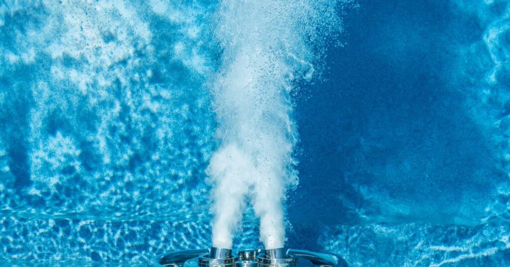 Close-up to the large metal jet of an endless pool with clear water producing two long rows of small bubbles.