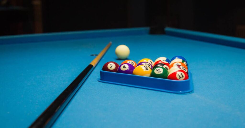 Close-up of the blue smooth surface of a pool table with a pool cue and pool balls inside the rack.