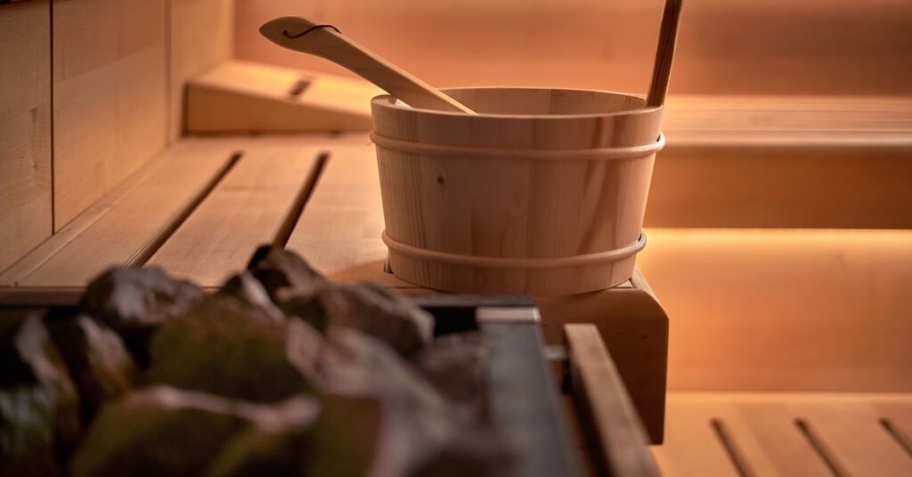 A sauna with a pile of rocks, a bucket with a ladle, and a strip of LED lights under the wrap-around benches.