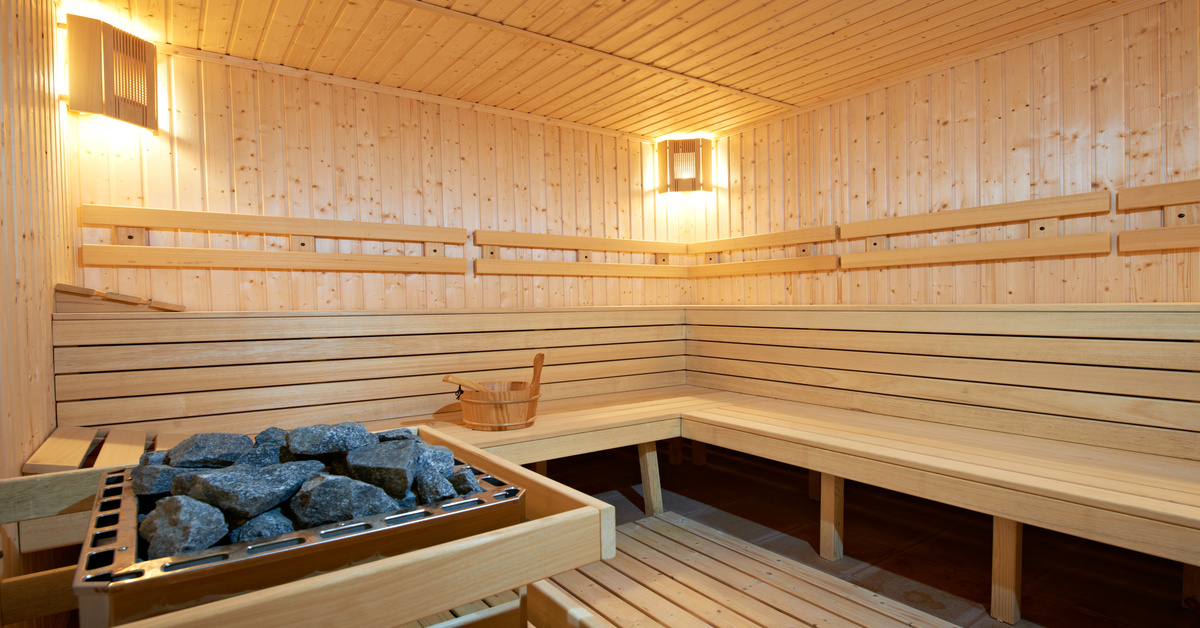 A sauna with lights in the corners, a raised square pit of black rocks, and a wooden bucket with a ladle.
