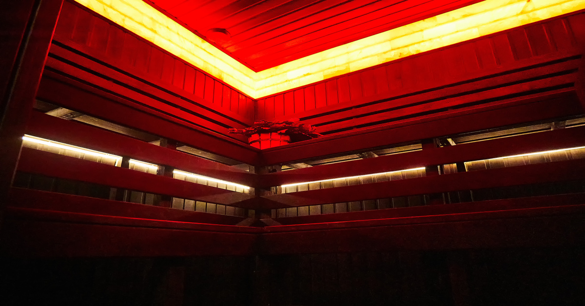The corner of the inside of an infrared sauna, with wooden walls, a wood bench, and red lights going around the ceiling.