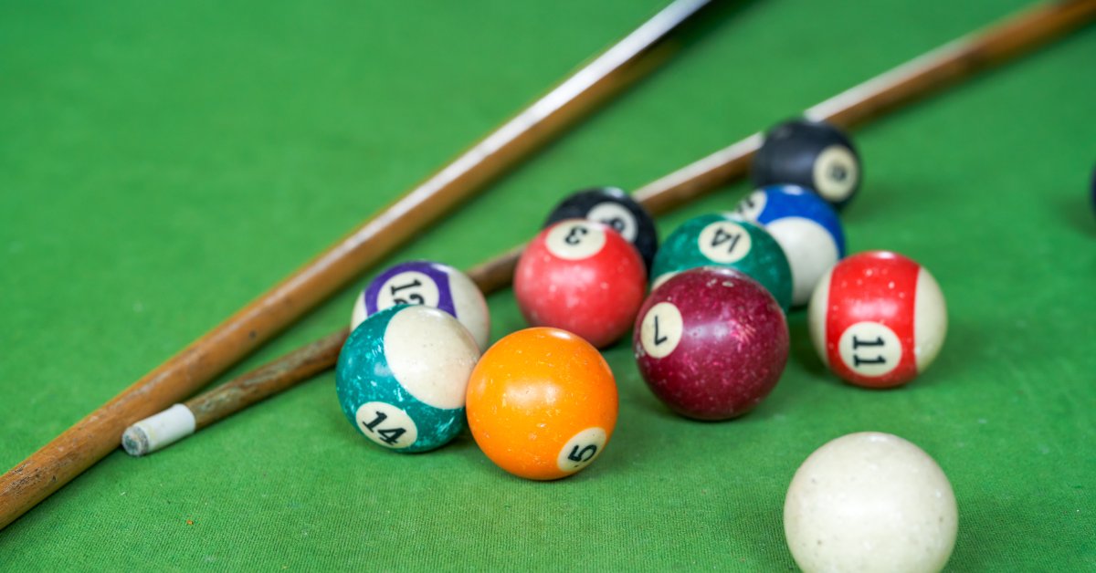 Two pool sticks and eleven billiards balls rest on a pool table with green felt.