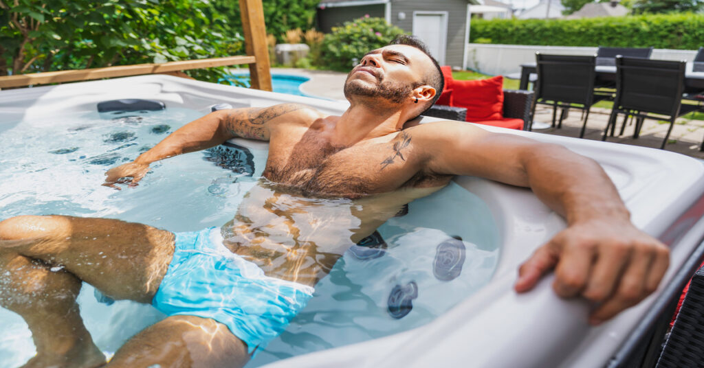 A man wearing blue swim trunks relaxes in front of the jets in a hot tub.