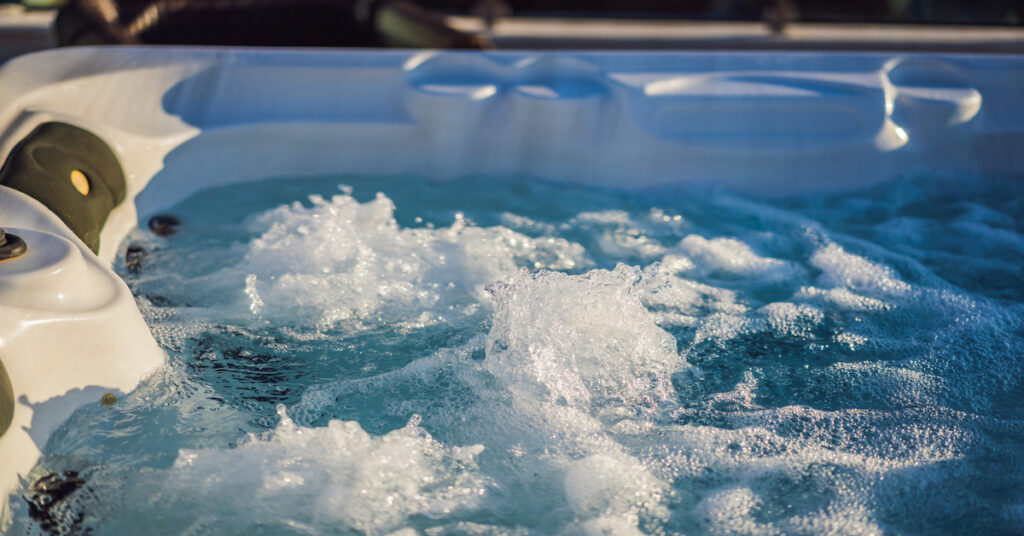 Blue water foams inside a white hot tub with jets on the side.