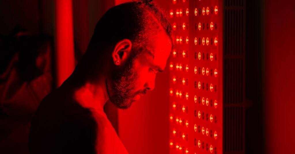 A man stands in front of an infrared feature on the wall of a sauna. The feature glows red.