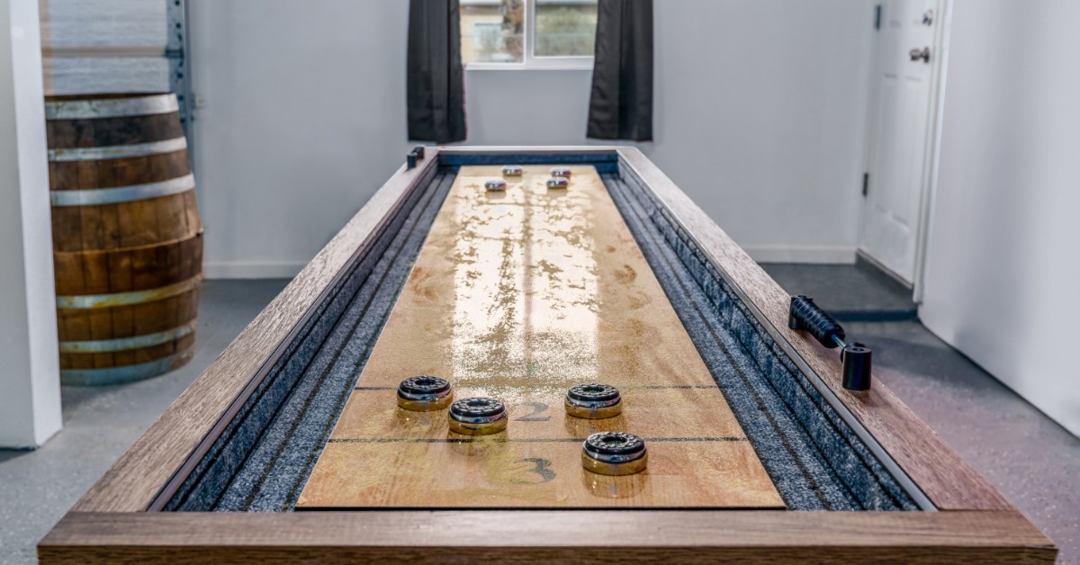 A wooden shuffleboard table in the center of an at-home game room.
