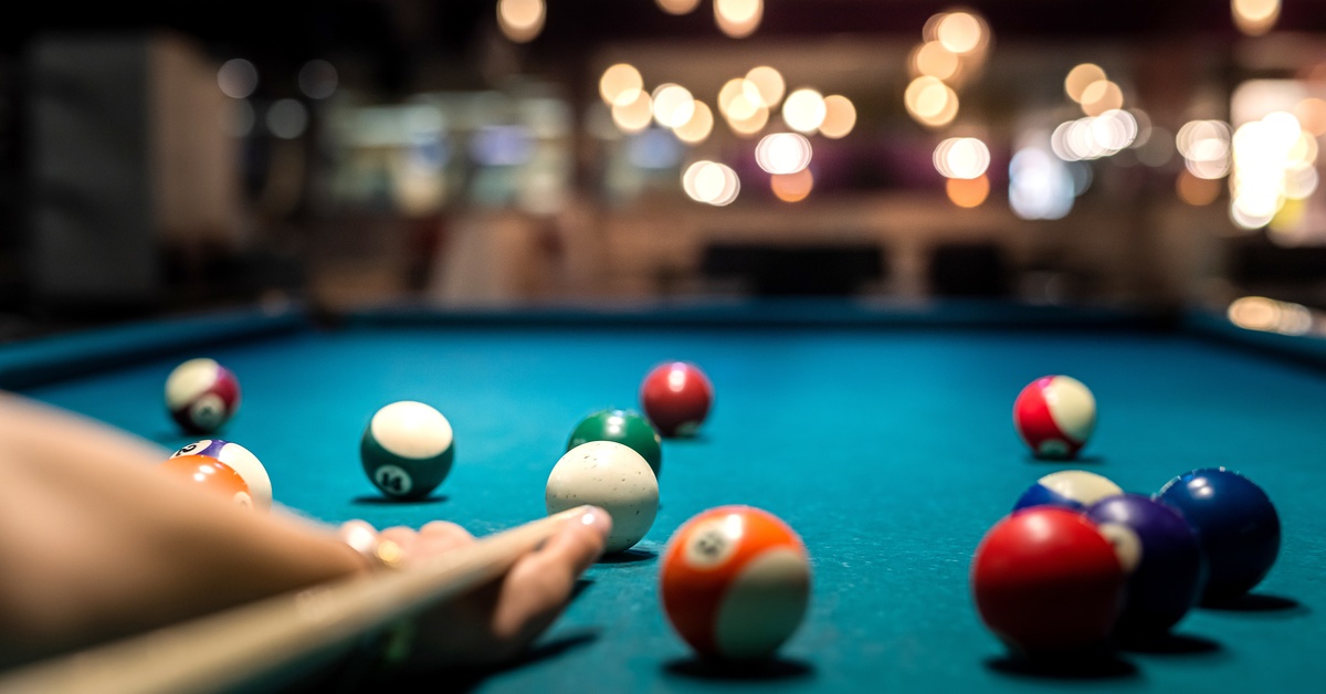 A person holding a pool stick as they prepare to hit the white cue ball on a green-felted billiards table.