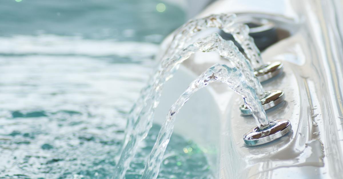 Water cascading from three stainless steel waterfall jets into a bubbling hot tub.
