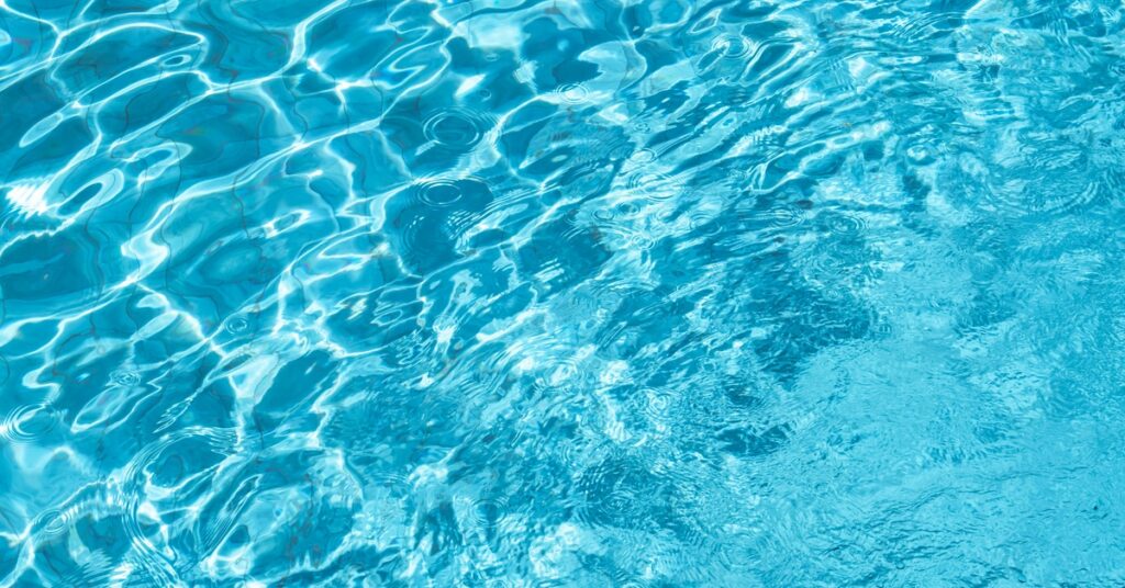 Clean, crystal-clear blue pool water with sunlight reflecting across the rippling surface.