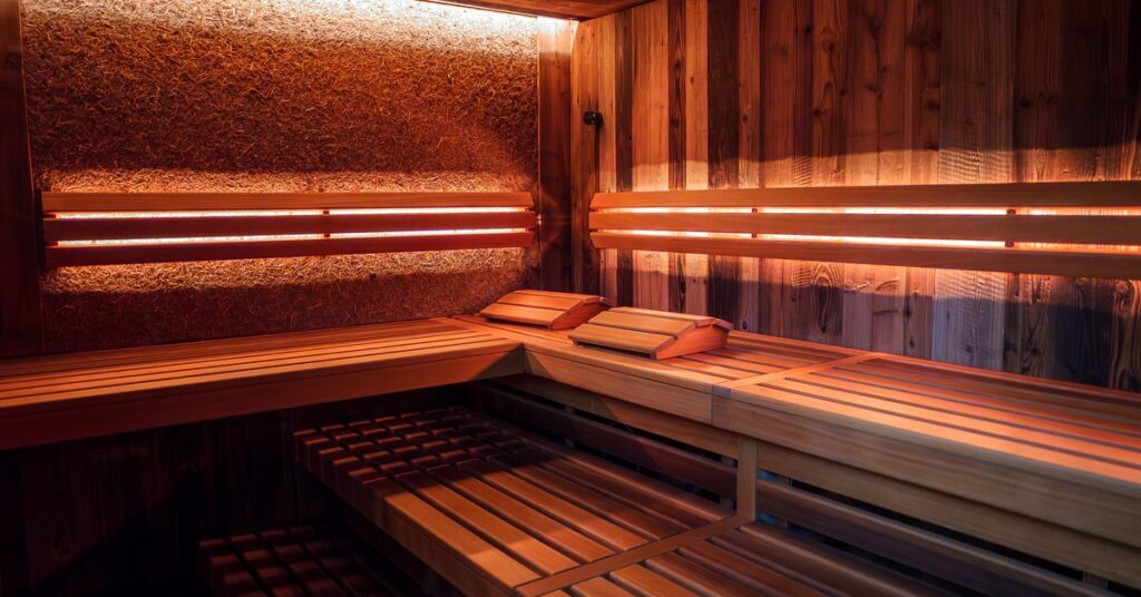The interior of a wooden sauna, with tiered wooden bench seating and infrared lighting.