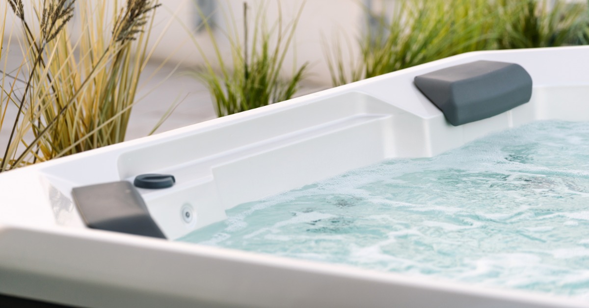 A white hot tub filled with water in a serene outdoor setting, with tall grass behind it.