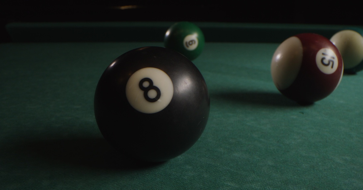 Four billiard balls resting on a green pool table, with the black 8-ball in focus and the other balls blurred in the background.