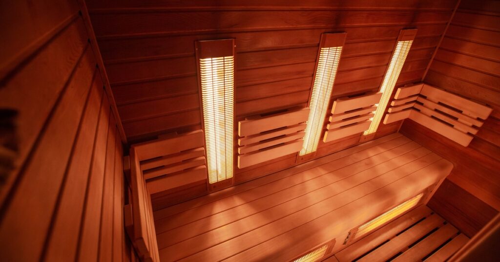 A modern infrared sauna with glowing wall-mounted heating panels, wooden bench seating, and warm ambient lighting.