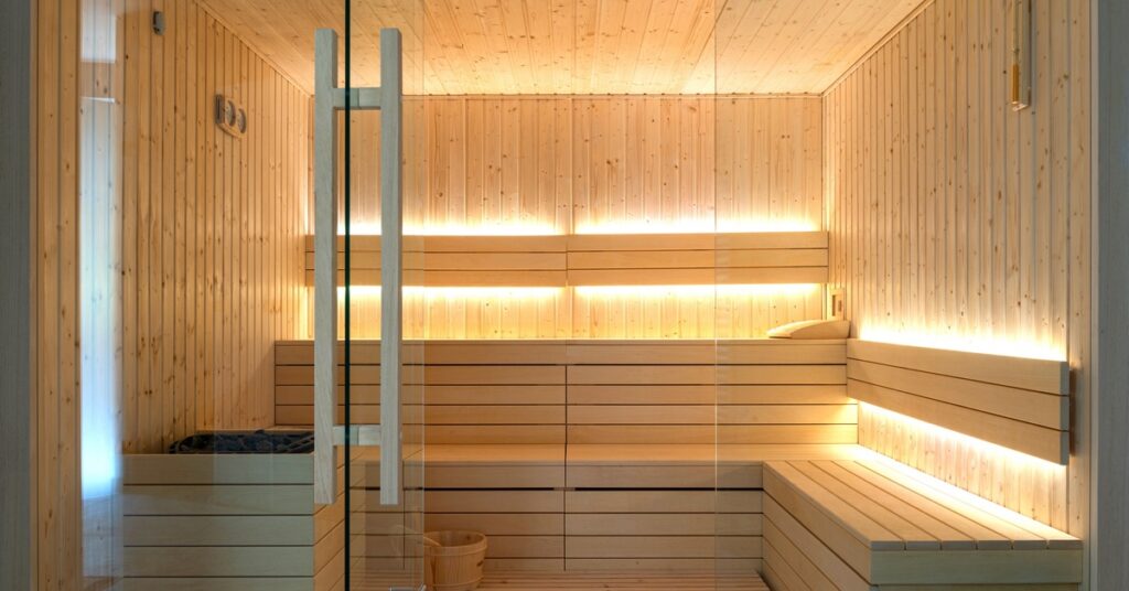 A traditional wooden sauna with tiered bench seating, soft LED accent lighting, and a glass entry door.