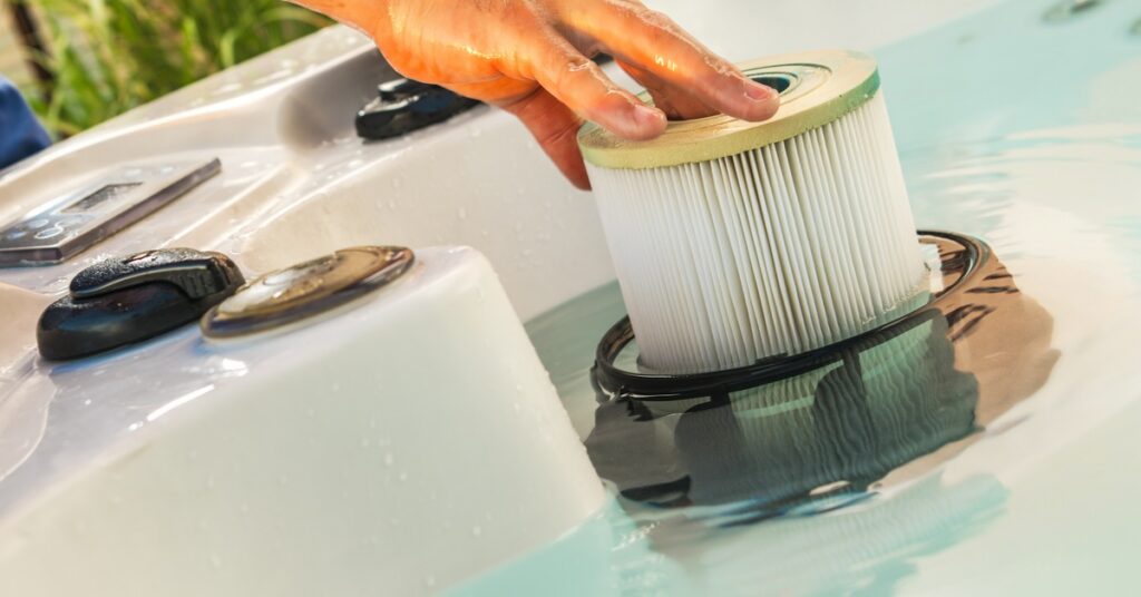 Someone’s hand removing a hot tub filter cartridge from spa water during routine maintenance.