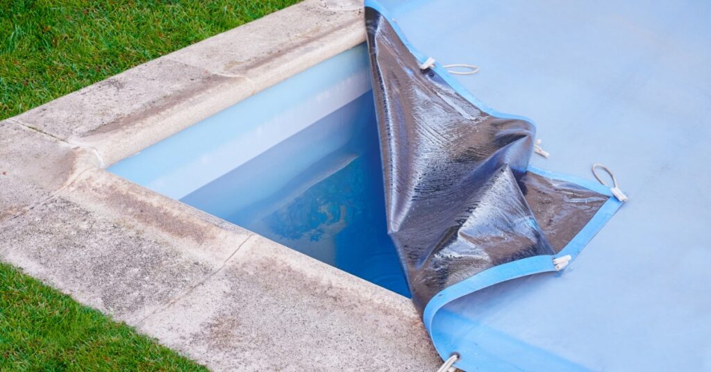 The corner of a swimming pool with a partially rolled-back blue cover, revealing clear water beneath.
