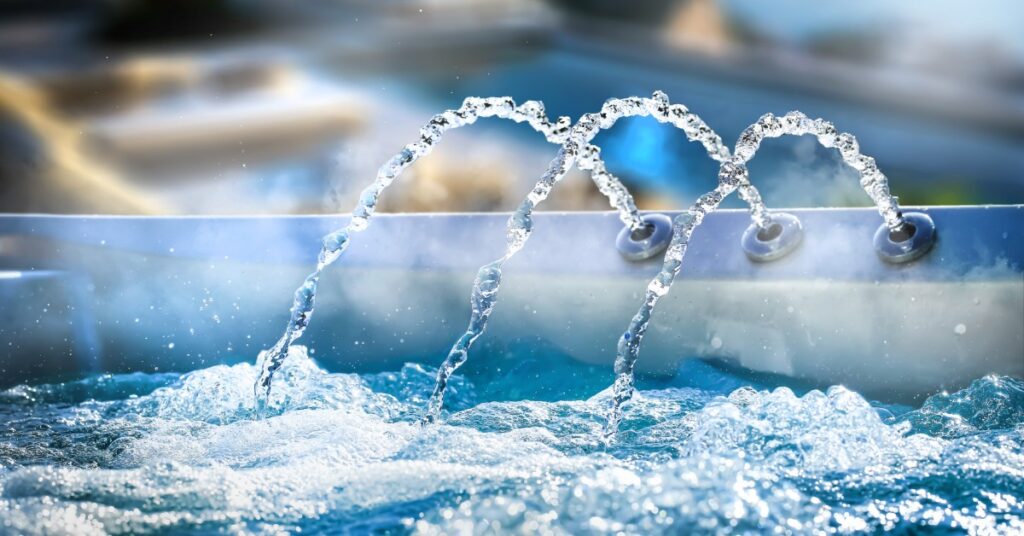 Hydrotherapy jets arcing into a bubbling outdoor hot tub with clear blue water.