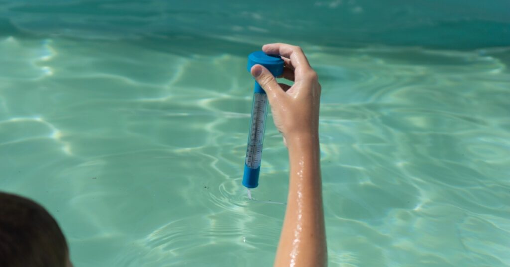 A person holding a floating water thermometer in a swim spa with blue-green water.