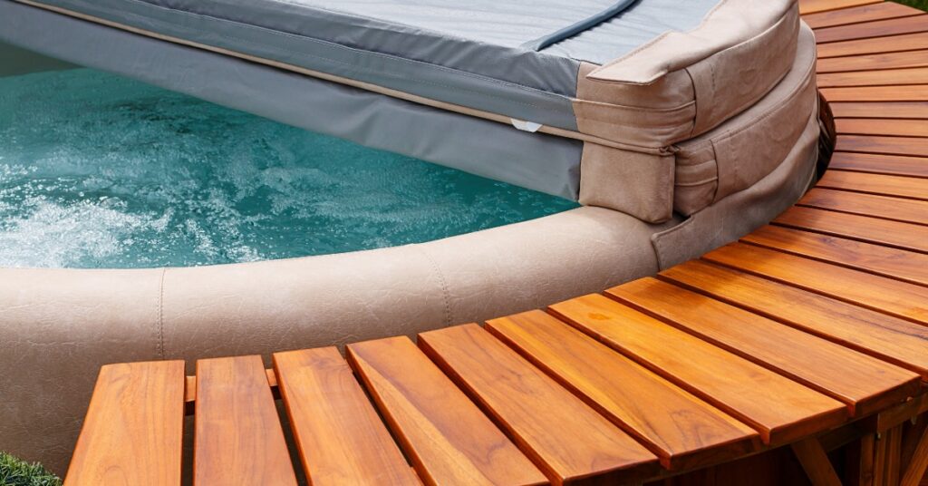 An insulated pool cover partially closed over a bubbling swim spa with a surrounding wooden deck.